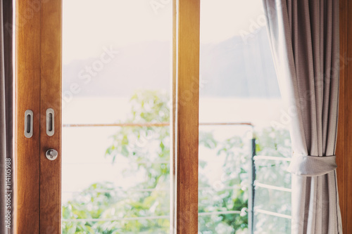 Wooden balcony door frame with curtain in the morning, with bright light, vintage tone