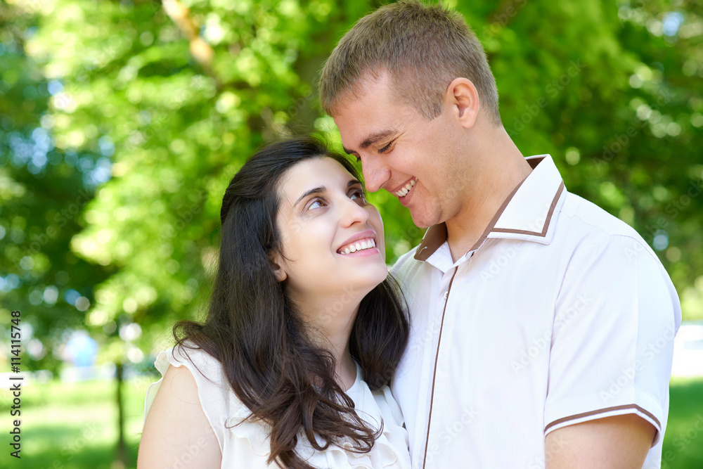 pregnant woman with husband posing in the city park, family portrait, summer season, green grass and trees pregnant woman with husband posing in the city park, family portrait, summer season, green grass and trees
