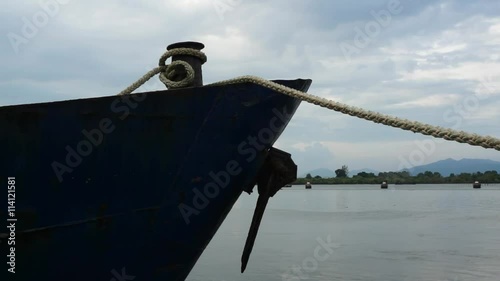 Bow of blue metal ship with rusty anchor moored at harbor dock.