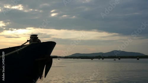 Bow of blue metal ship with rusty anchor moored at harbor dock at sunset.