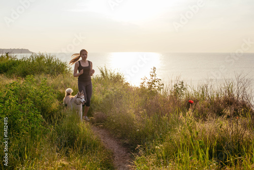Running woman. Female runner jogging with siberian husky dogs during the sunrise on beach.