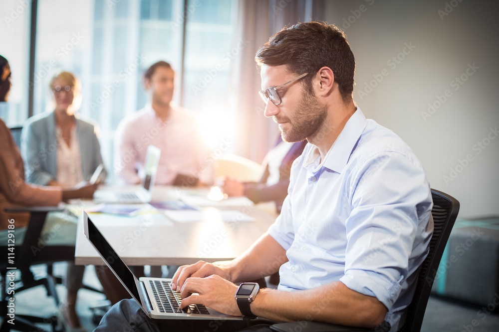 Man using laptop while coworker interacting in the background Man using laptop while coworker interacting in the background