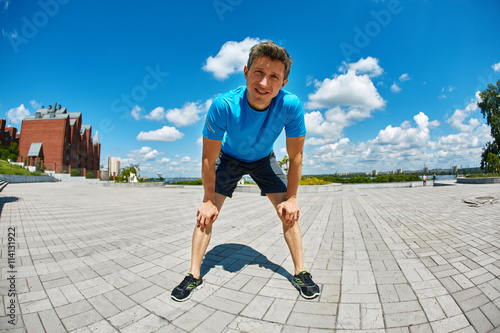 man runner athlete warming up and stretched before jogging along a city bay at the early morning. man fitness sunset jogging workout wellness concept. man funny looks in the frame, photographed on a