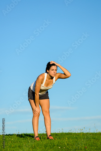 Tired young woman taking a running workout rest. Motivated female athlete on an exercising break for breathing. Motivation and healthy fitness lifestyle concept.