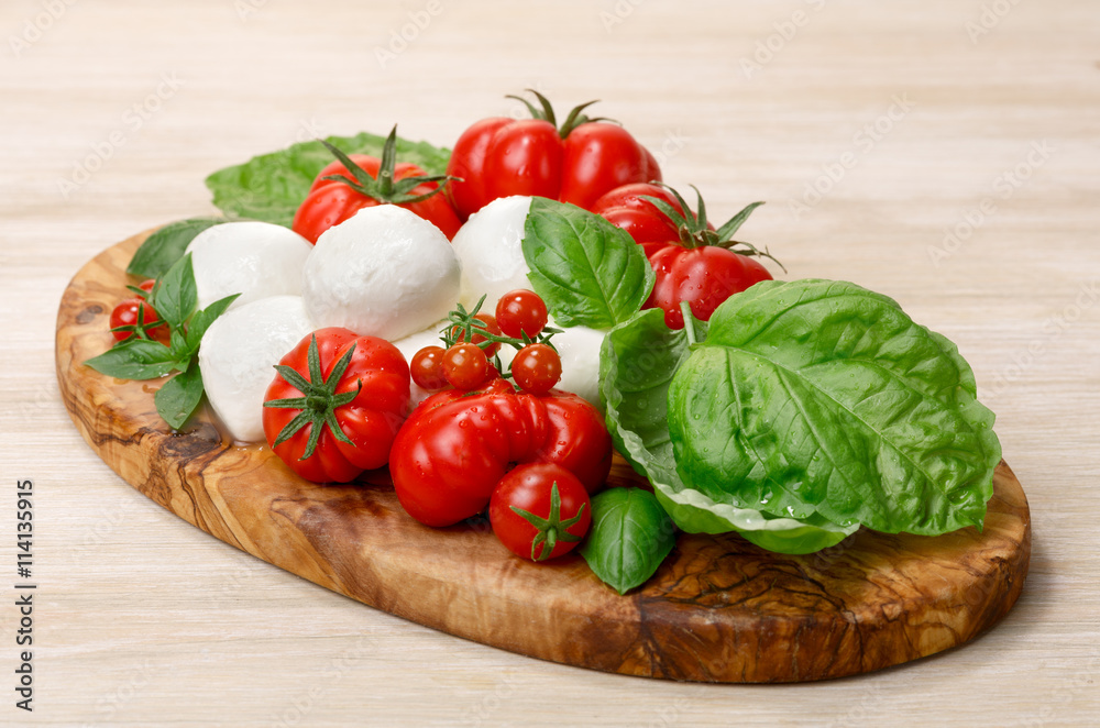 Mozzarella, heirloom tomatoes, basil leaves on a wooden serving Mozzarella, heirloom tomatoes, basil leaves on a wooden serving