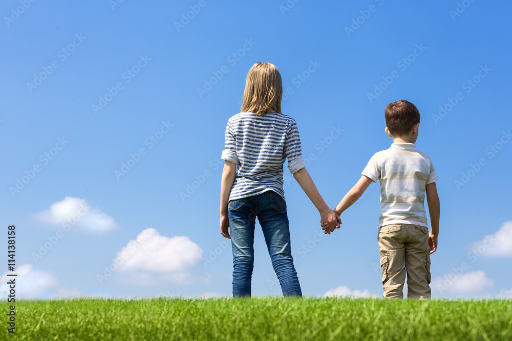 Brother and sister holding hand on grass at background of sky Brother and sister holding hand on grass at background of sky