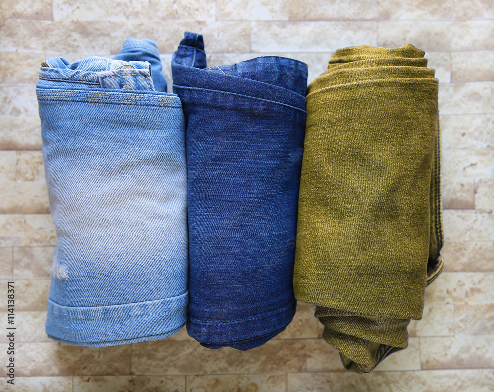 Fashionable stack of jeans, trouser, clothes on a texture backgr Fashionable stack of jeans, trouser, clothes on a texture backgr