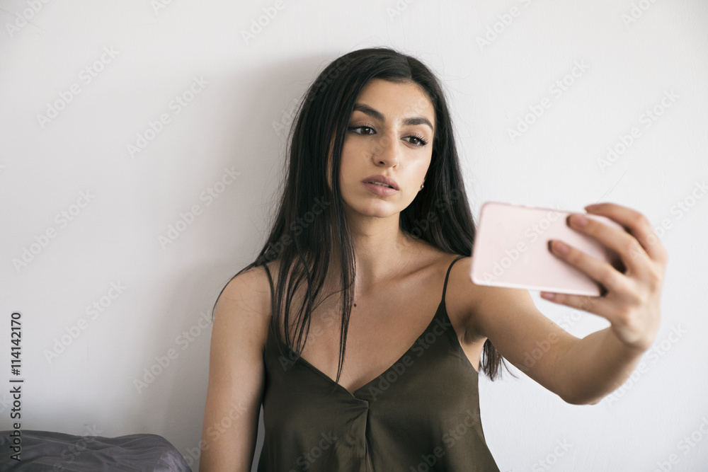 Φωτογραφία Black-haired girl in night gown taking selfie in morning bedroom