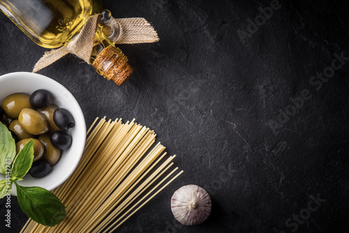 Spaghetti, olives and olive oil on the black stone table