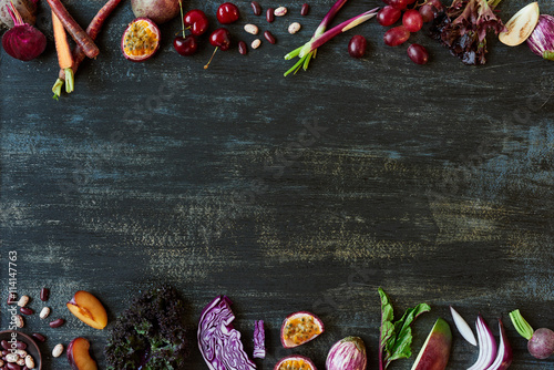 Border of purple colored fruit and vegetables on dark rustic bac