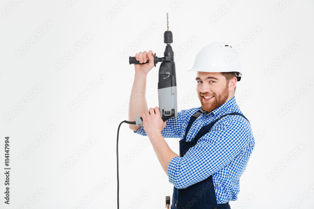 Cheerful young worker in helmet using drill and pointing up Cheerful young worker in helmet using drill and pointing up