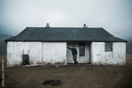 Hiker leaning against a wall of the shelter house at the Camasunary Bothy in the Scottish Highlands, Isle of Skye, Scotland photo