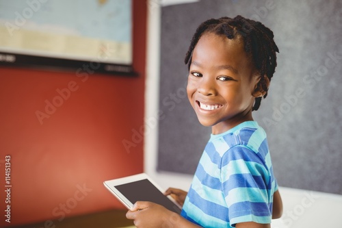 Portrait of schoolboy holding digital tablet in classroom