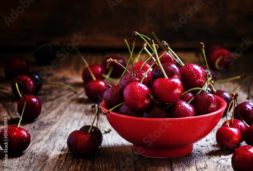Red sweet cherry in a red bowl , dark vintage wooden background,