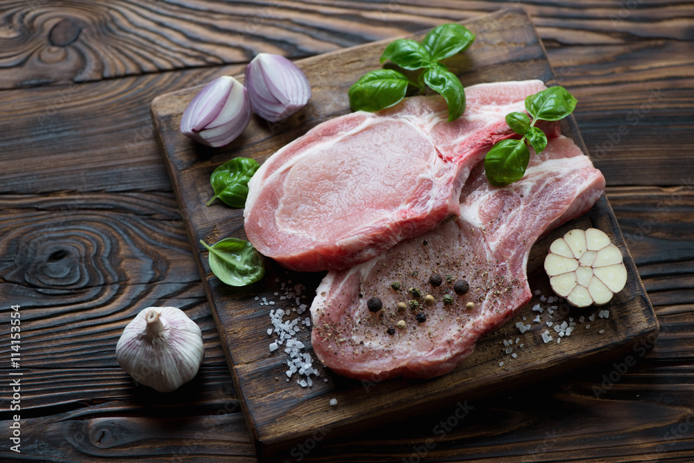 Raw fresh pork chop steaks and seasonings, rustic wooden setting