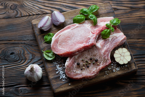 Raw fresh pork chop steaks and seasonings, rustic wooden setting