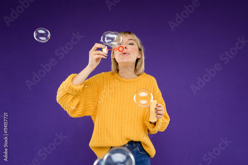 Portrait of young girl blowing bubbles over purple background.