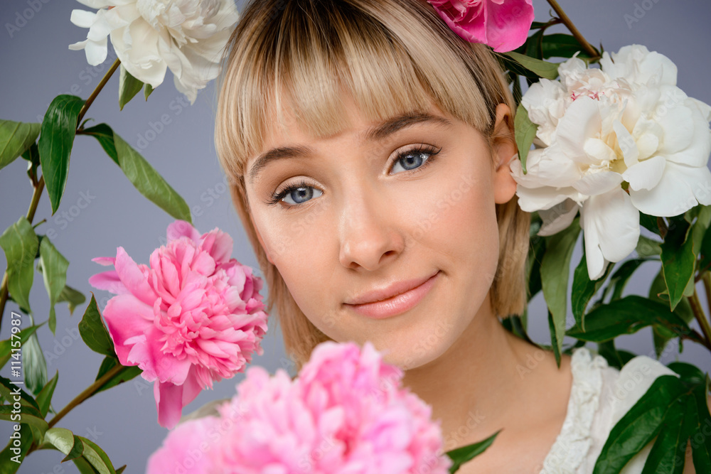 Portrait of young girl among flowers over grey background. Portrait of young girl among flowers over grey background.