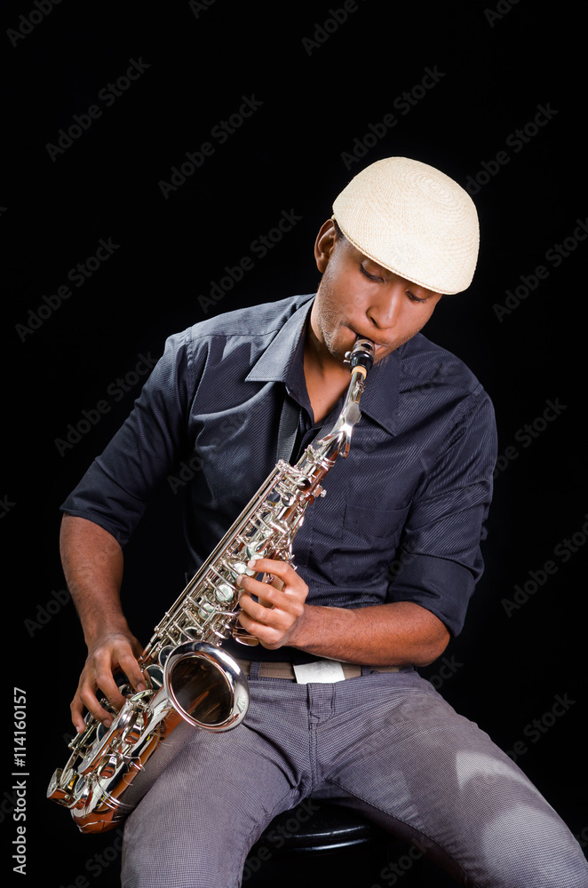 Naklejka premium With white hat a black man is sitting and playing his saxophone, dark background, nice music