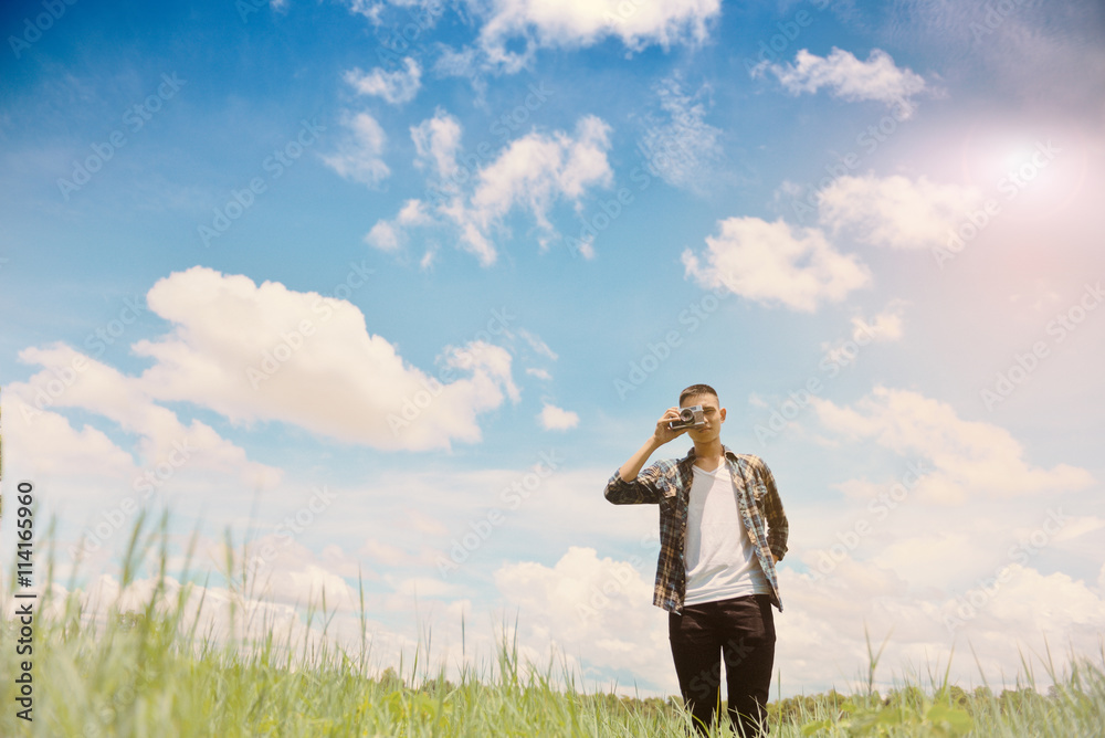 Young man with camera at meadow against sky.Man standing on gree Young man with camera at meadow against sky.Man standing on gree