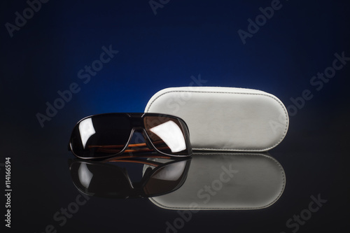 Elegant sunglasses and case on black background with blue light