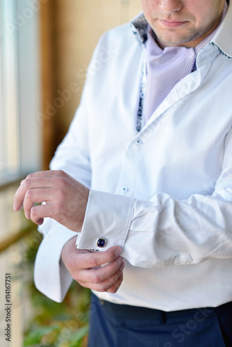 Groom is wearing cuff-links indoors. Male portrait of handsome guy. Beautiful model boy in colorful wedding clothes. Man is posing