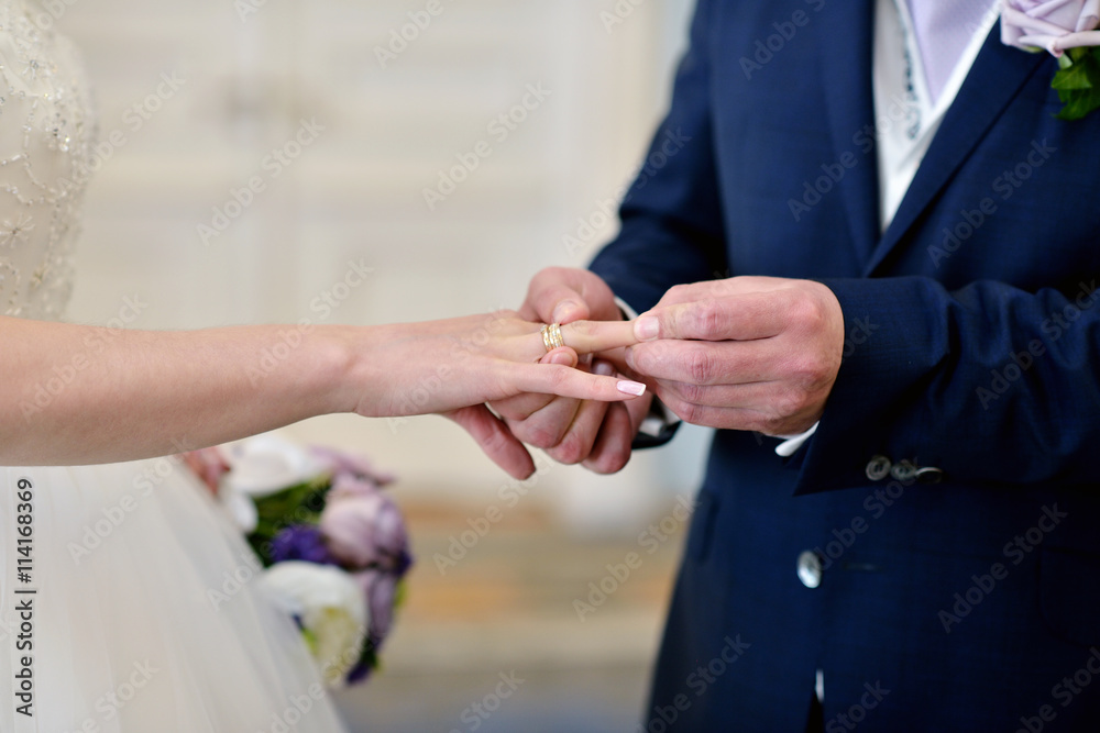 Beauty bride and handsome groom are wearing rings each other. Wedding couple on the marriage ceremony. Beautiful model girl in white dress. Man in suit. Female and male portrait. Cute lady and guy