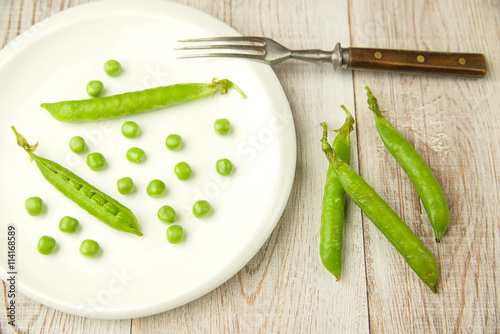 Pea pods and pea seeds on white plate