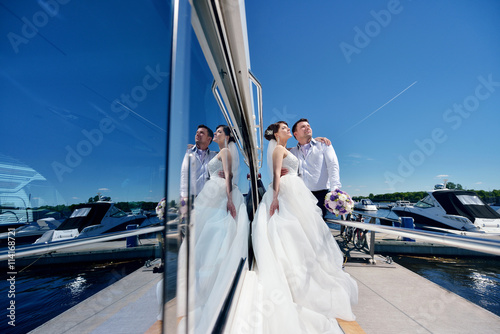 Wedding couple is hugging on a yacht. Beauty bride with groom. Beautiful model girl in white dress. Man in suit. Female and male portrait. Woman with lace veil. Cute lady and guy outdoors © pvstory