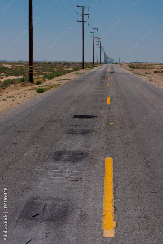 Fototapeta premium A road with a dashed yellow line leads to the horizon in the desert.