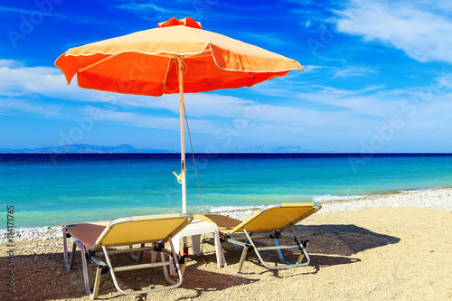 colorful beach umbrellas with deck chairs pebble beach and island in the distance