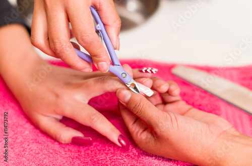 Closeup females hands getting manicure treatment from woman using nail scissors in salon environment  pink towel surface  blurry background products