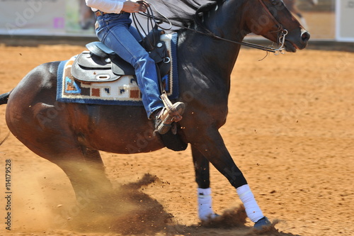 The side view of the rider in leather chaps sliding his horse forward and raising up the 