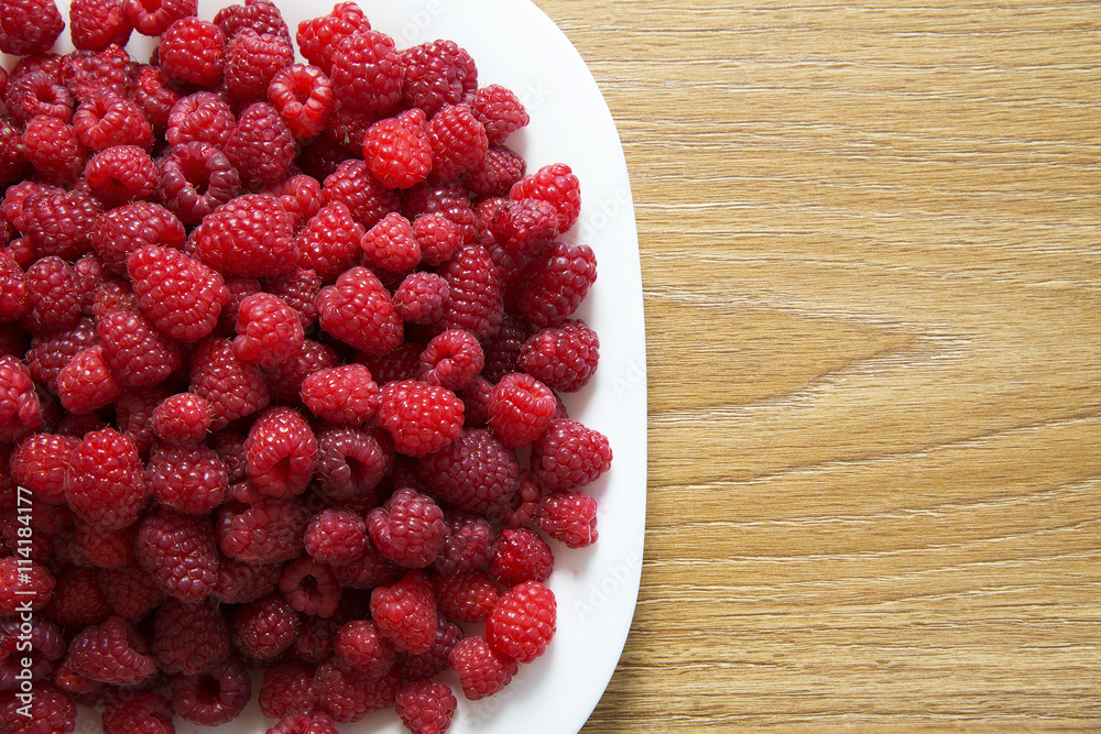 Fresh raspberries in a white plate on a wooden table Fresh raspberries in a white plate on a wooden table