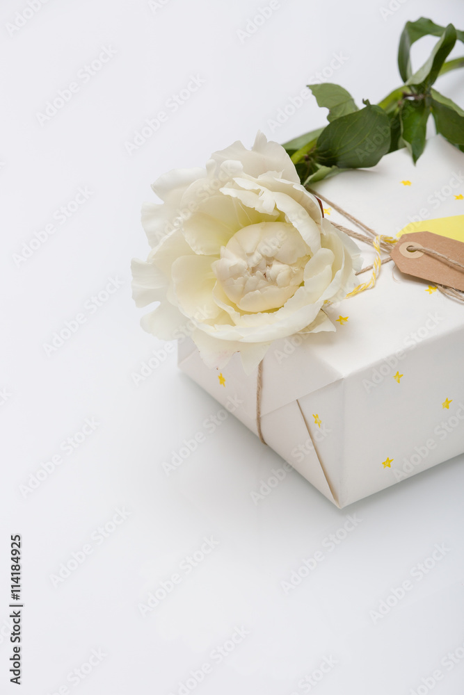 Nice present packed in white paper with small yellow stars with beautiful peony flower on white wooden background. Wrapped gift for birthday party. Mock-up. Holidays concept. Nice present packed in white paper with small yellow stars with beautiful peony flower on white wooden background. Wrapped gift for birthday party. Mock-up. Holidays concept.