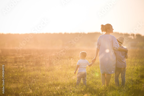 Beautiful young woman with two boys on the daisy meadow on a sunny day. Happy family on summer sunset. Kid boy, toddler and mom. Mum with baby and kid. Family and lifestyle concept