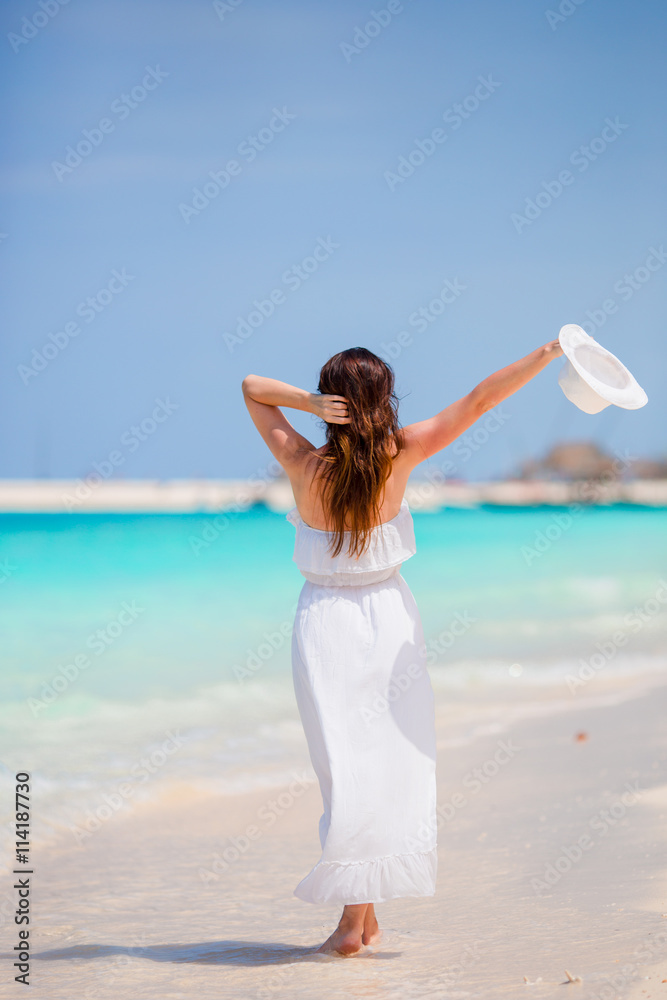 Young beautiful woman on beach vacation. Happy girl enjoy beach and warm weather while walking along the ocean Young beautiful woman on beach vacation. Happy girl enjoy beach and warm weather while walking along the ocean