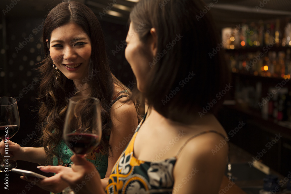 Young women looking at a smart phone with a glass of wine at the bar Young women looking at a smart phone with a glass of wine at the bar