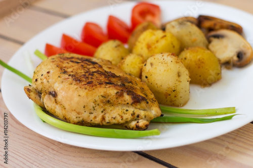 fried chicken fillet with potatoes tomatoes and mushrooms. on a wooden background