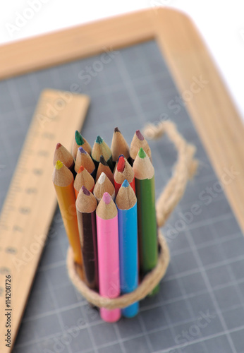 crayons de couleurs ficelés sur une ardoise avec une règle sur fond blanc