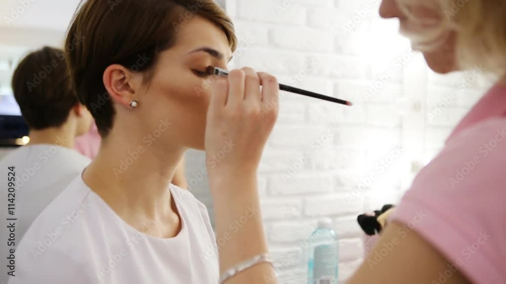 Portrait of beautiful young brunette woman with esthetician making makeup eye shadow Portrait of beautiful young brunette woman with esthetician making makeup eye shadow