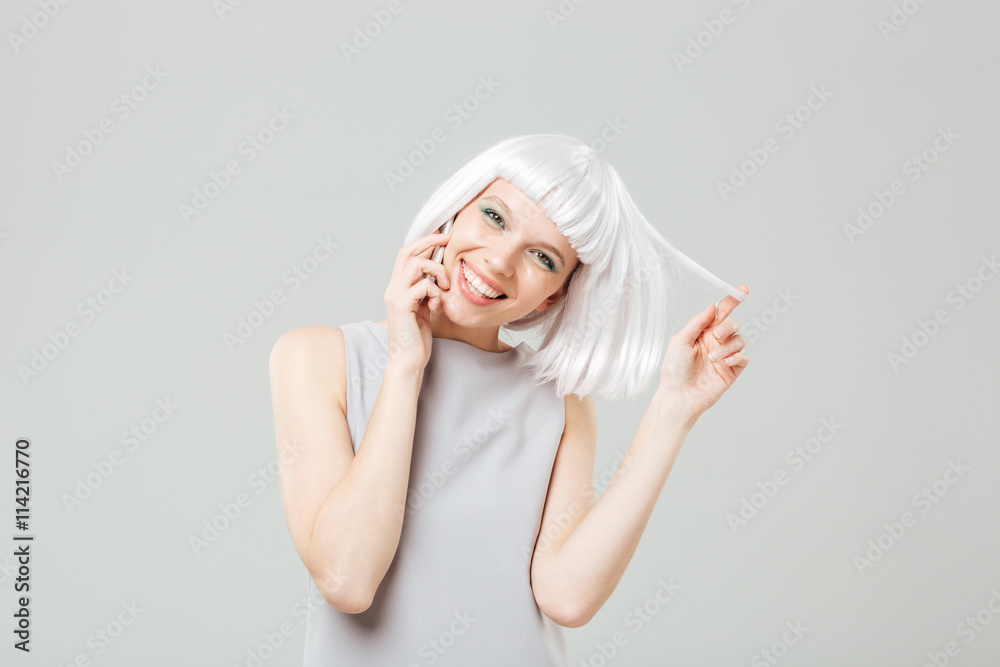 Cheerful playful woman in blonde wig talking on mobile phone Cheerful playful woman in blonde wig talking on mobile phone