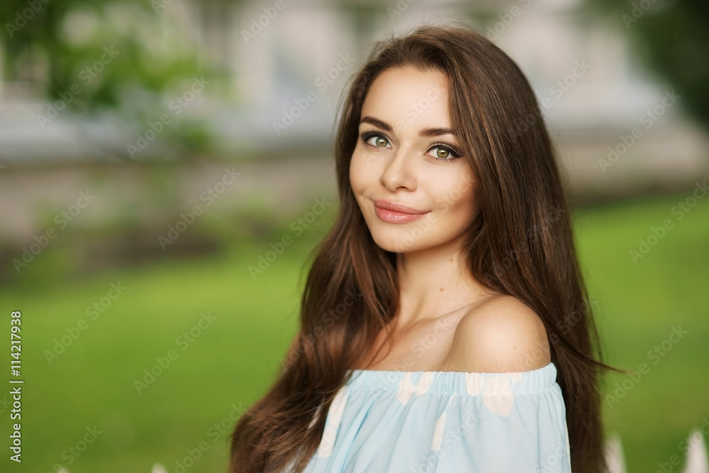Obraz premium Young beautiful woman with long brunette hair. Calm girl with perfect clean skin posing in park and looking in camera