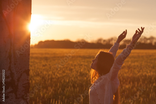 woman with open arms in the green wheat field at the morning.