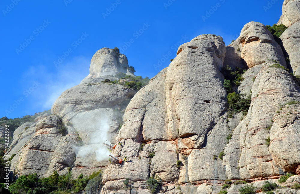 Workmen drilling the limestone cliffs of the mountains of Montserrat, Catalonia, Spain