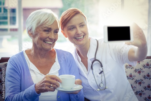 Smiling doctor and patient looking at phone while having tea