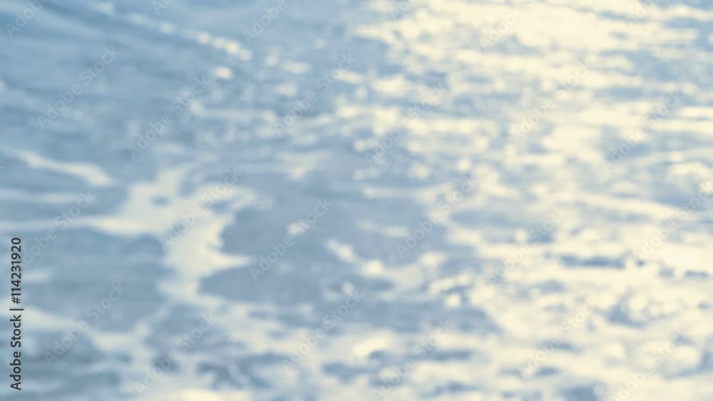 Sunlight sparkling on the water surface, waves rolling on a beach - slow motion - loop