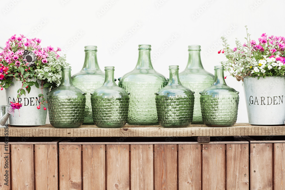 Flowers in a bucket, glass vintage bottles on wooden background,
