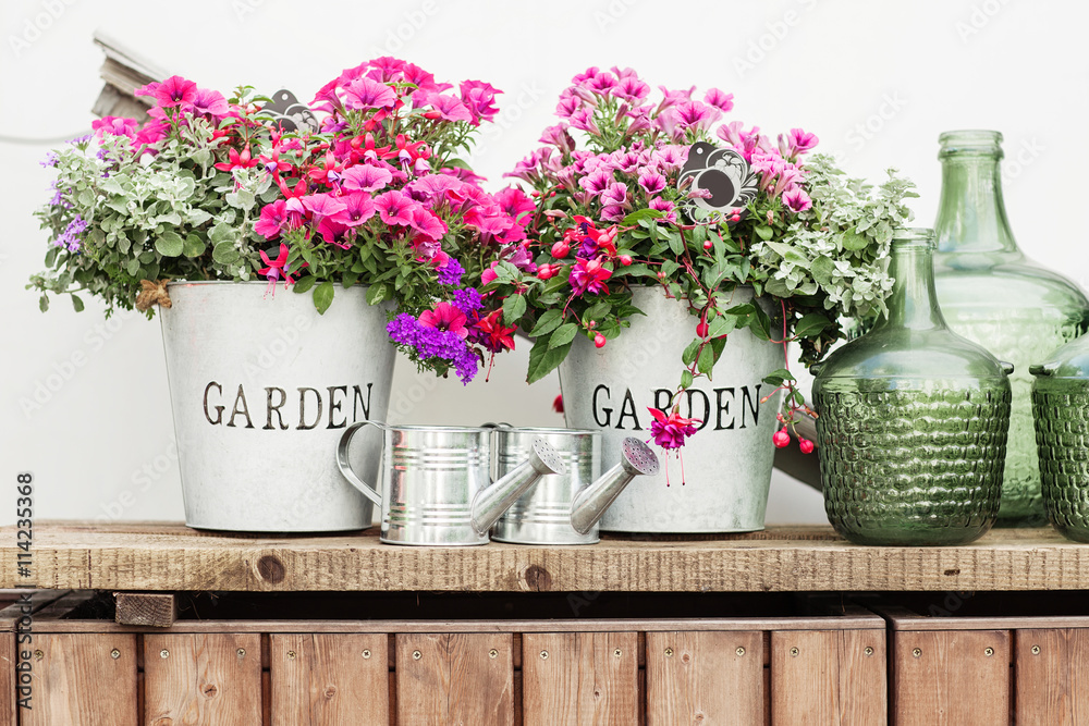 Flowers in a bucket, glass vintage bottles on wooden background,