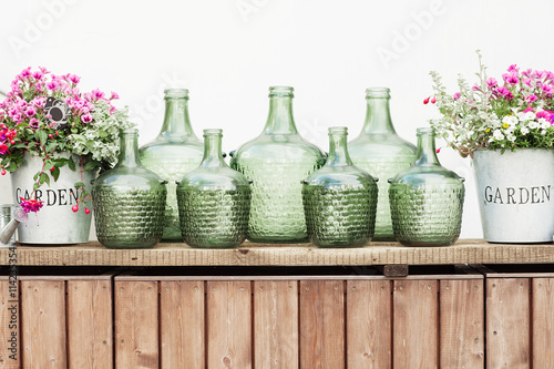 Obraz na płótnie Flowers in a bucket, glass vintage bottles on wooden background, w salonie